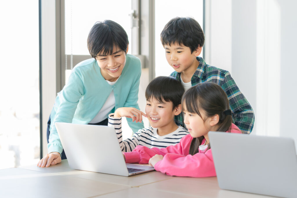 子供三人がパソコンの前で先生に教えてもらう